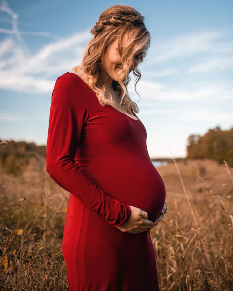 Expecting mother in a fitted red maternity gown in a field